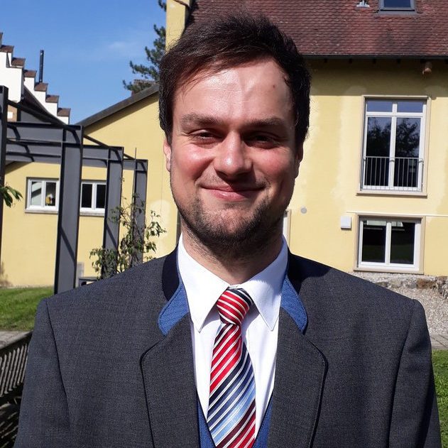 1. Vorstand David Graf. Ein Mann in Uniform des Musikverein Rheinheim lächelt vor einem gelben Gebäude im Freien.