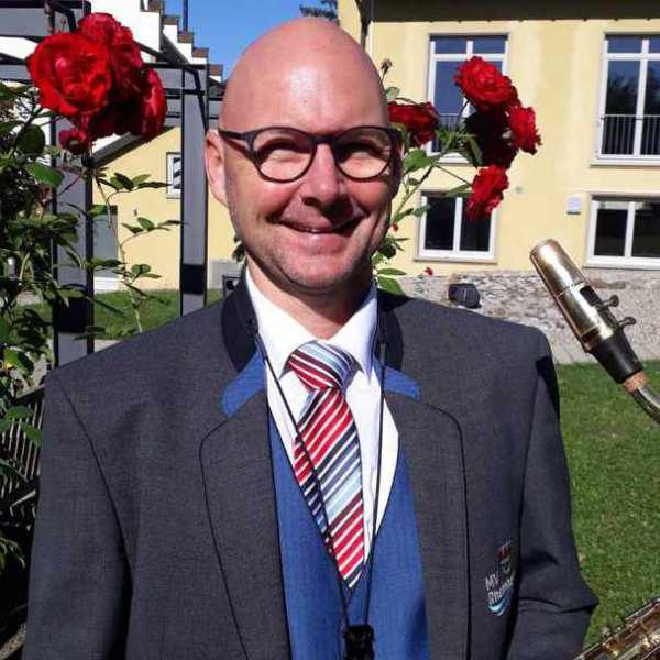 Jens Noack, Kassierer. Mann mit Brille in Uniform des Musikverein Rheinheim lächelt vor einer Umgebung mit roten Rosen.